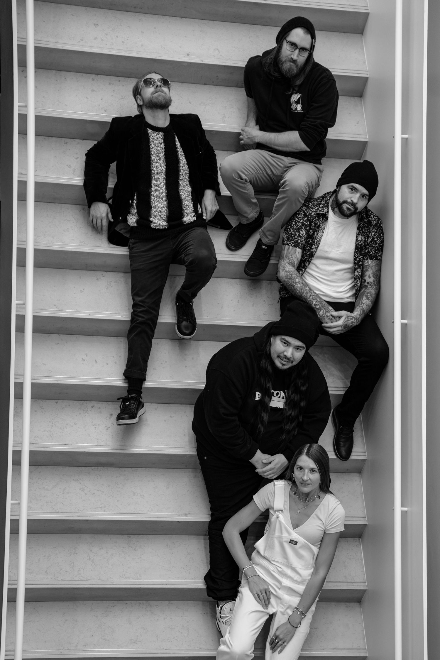Group portrait of band members sitting on white stairs in casual attire.