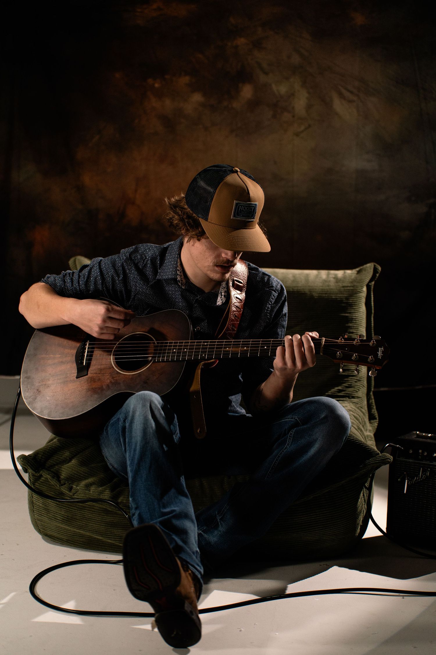 Musician plays acoustic guitar while lying down in moody studio lighting.