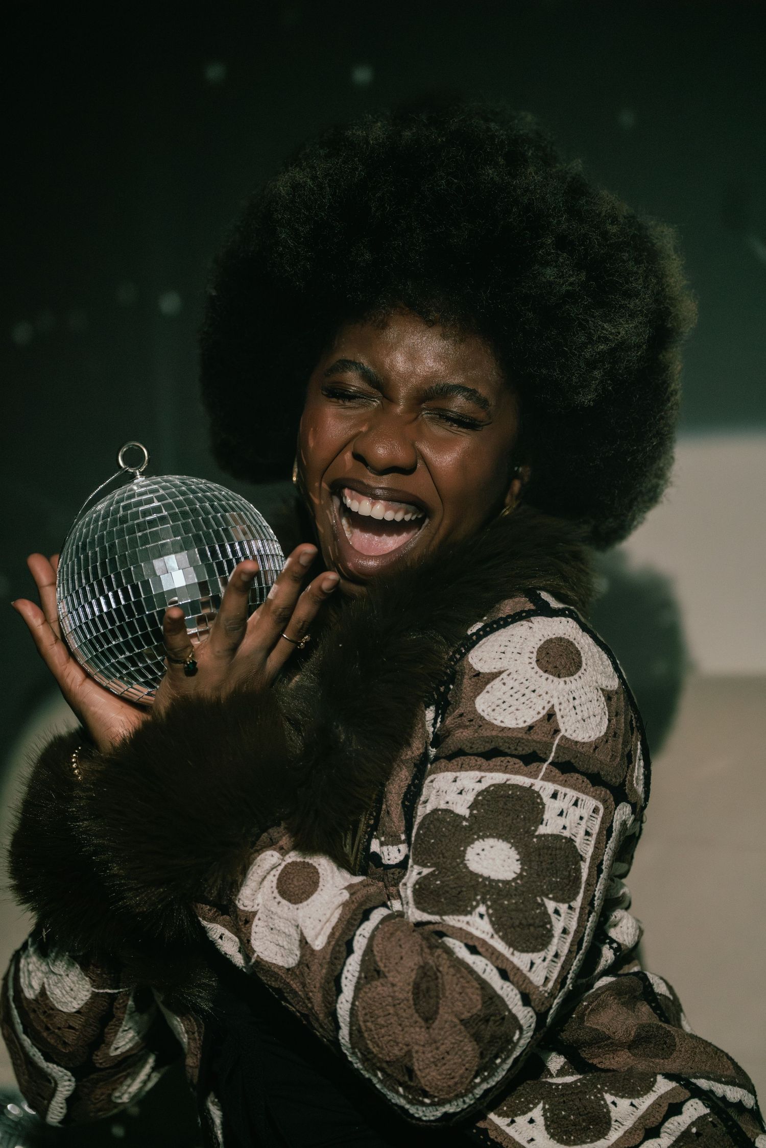 Retro styled portrait with disco ball and floral print sweater capturing joy and 70s fashion.