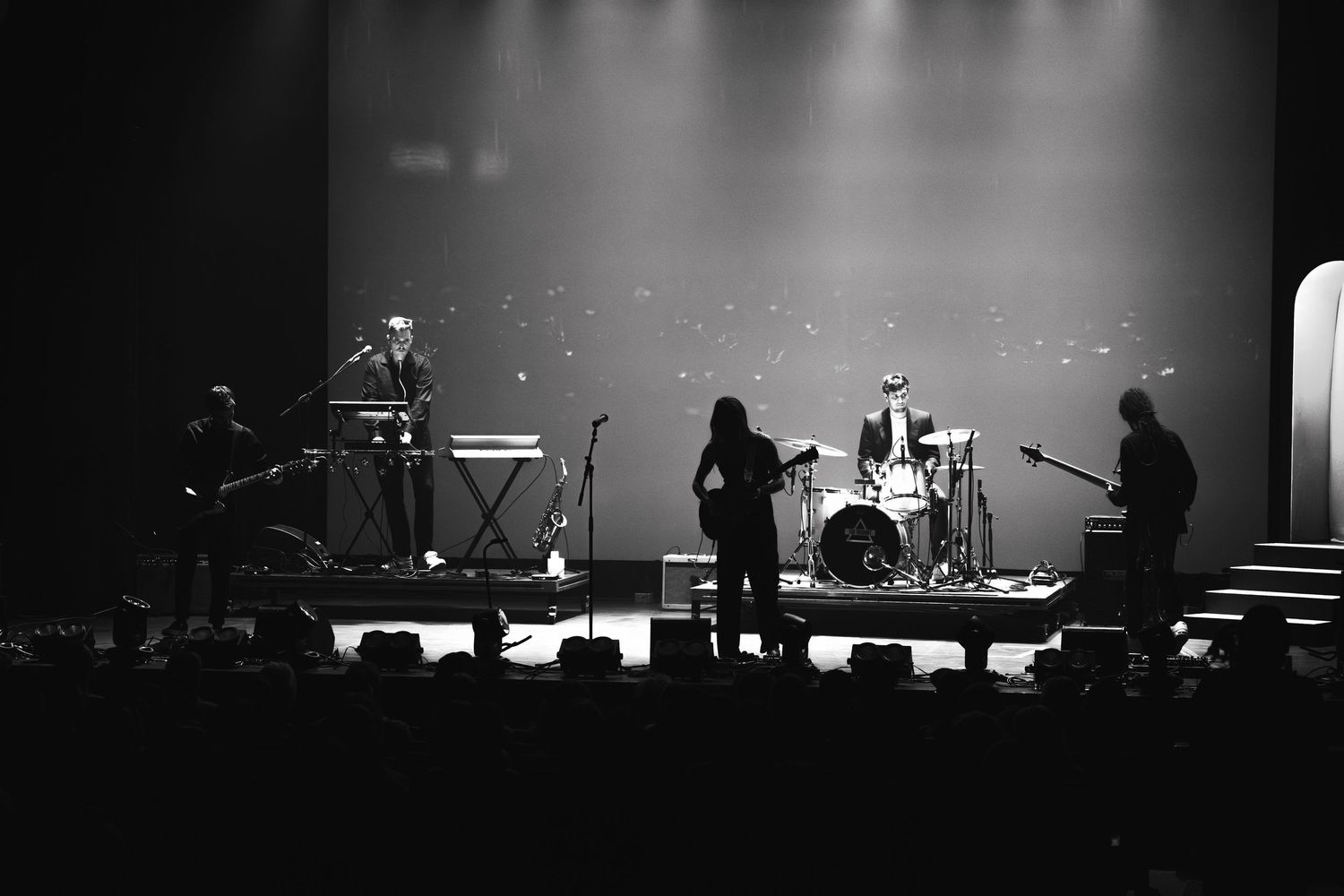 Black and white concert photo showing band performing on stage with dramatic lighting.