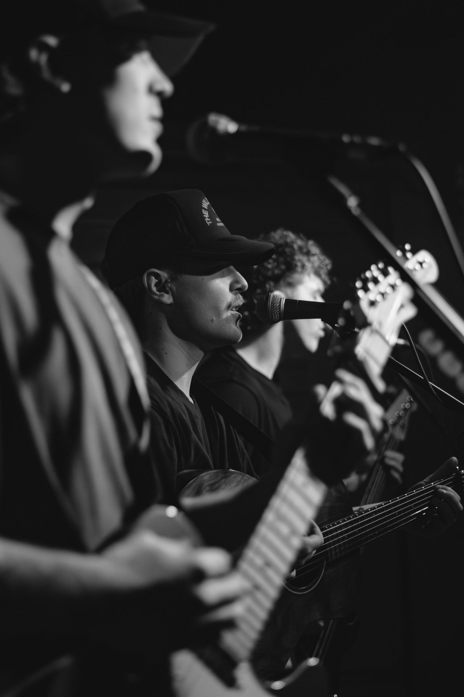 Black and white photo of musicians performing in line on dimly lit stage.