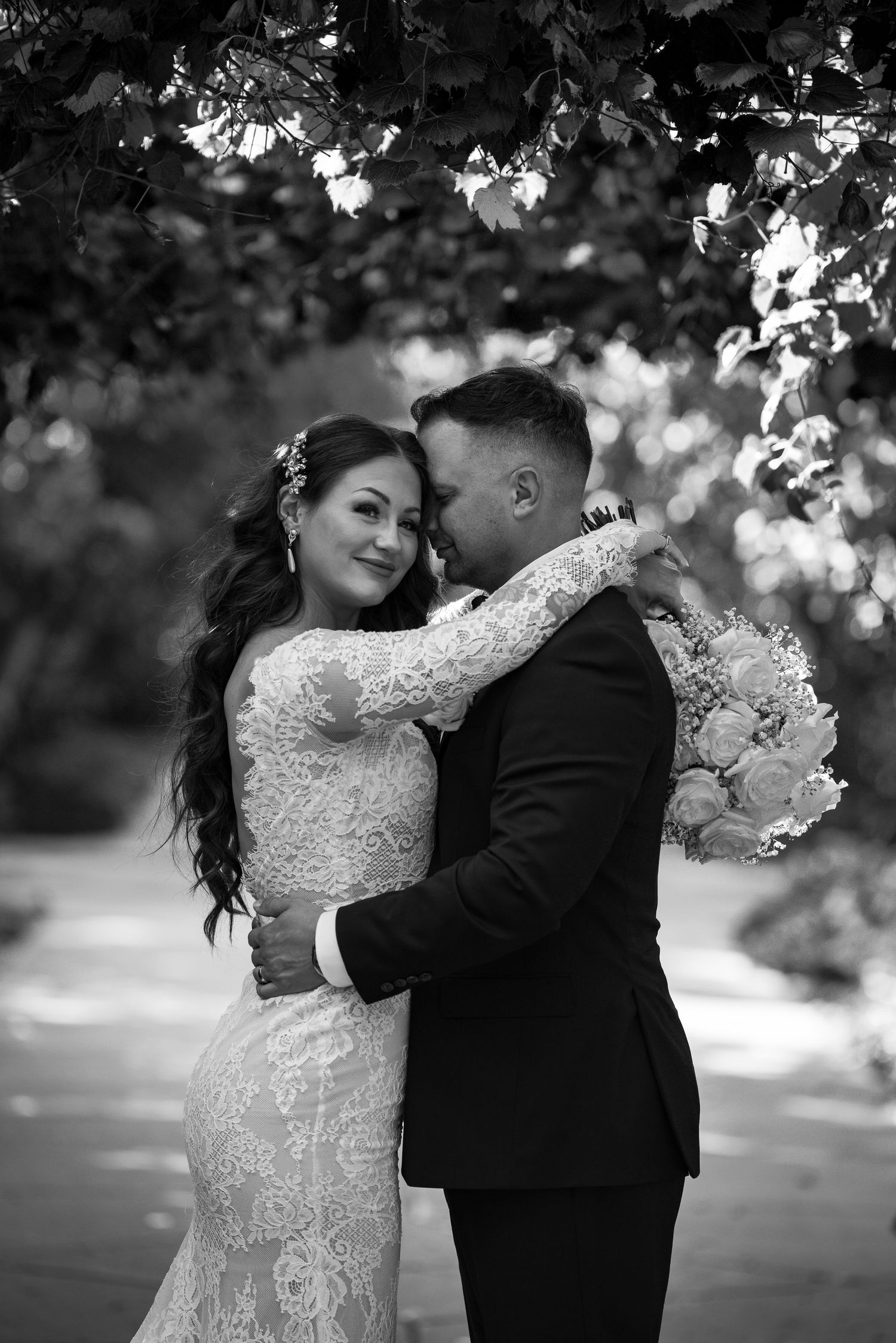 Elegant black and white wedding photo showing couple embracing outdoors with floral bouquet.