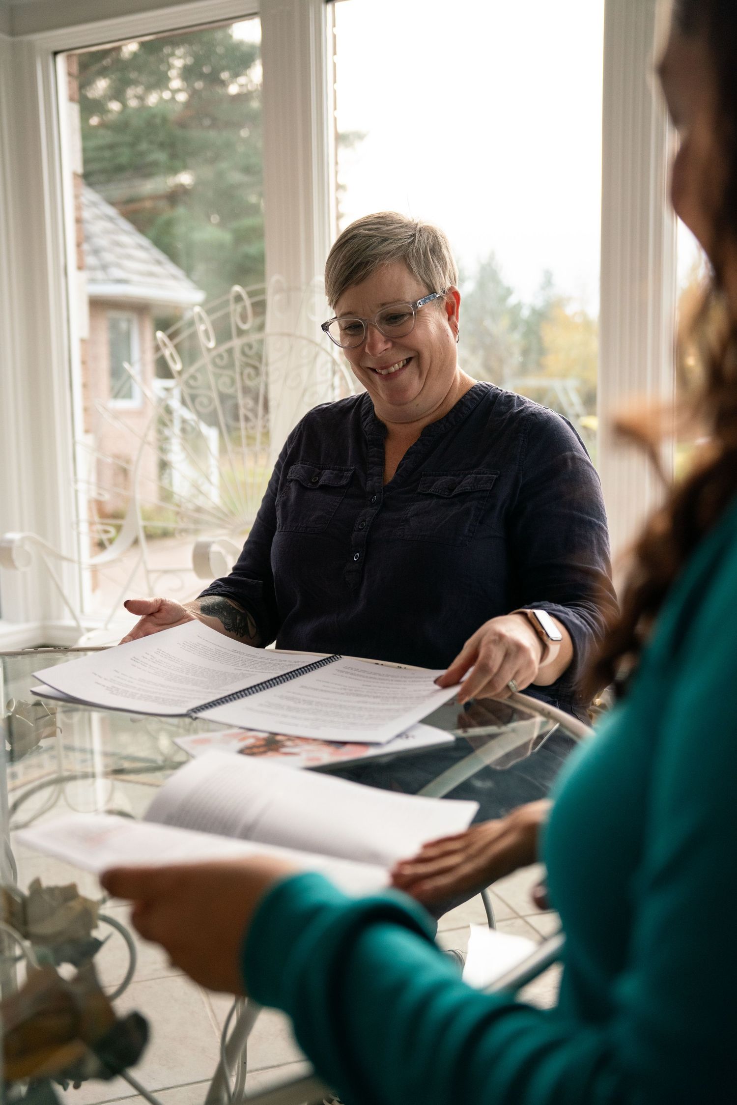 Business meeting showing paperwork review in a bright sunlit room with windows.