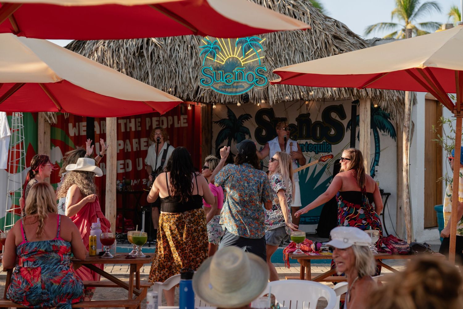 Thatched roof beach bar with red umbrellas and ocean views.