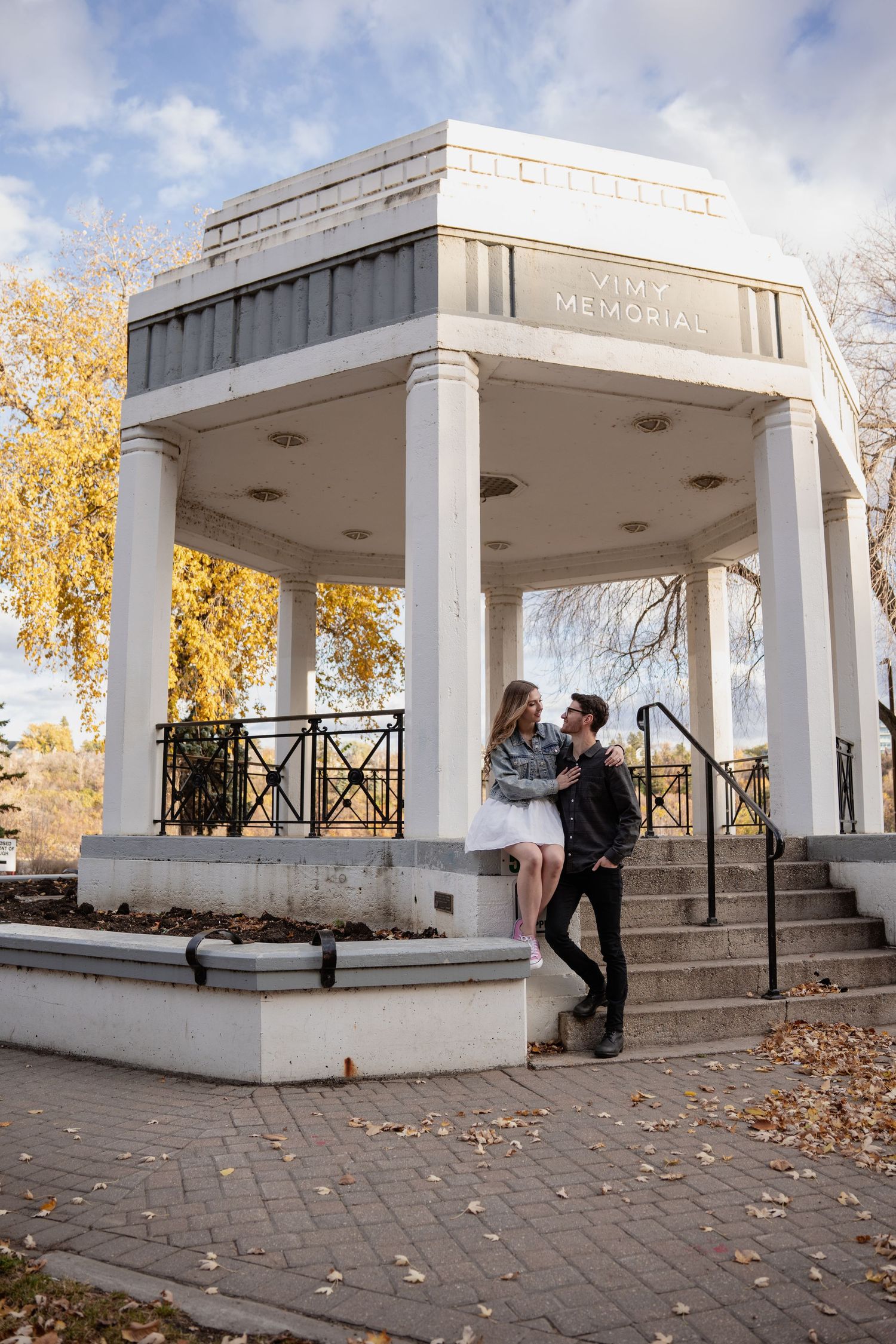 White columned pavilion in a park with fallen autumn leaves on the ground.
