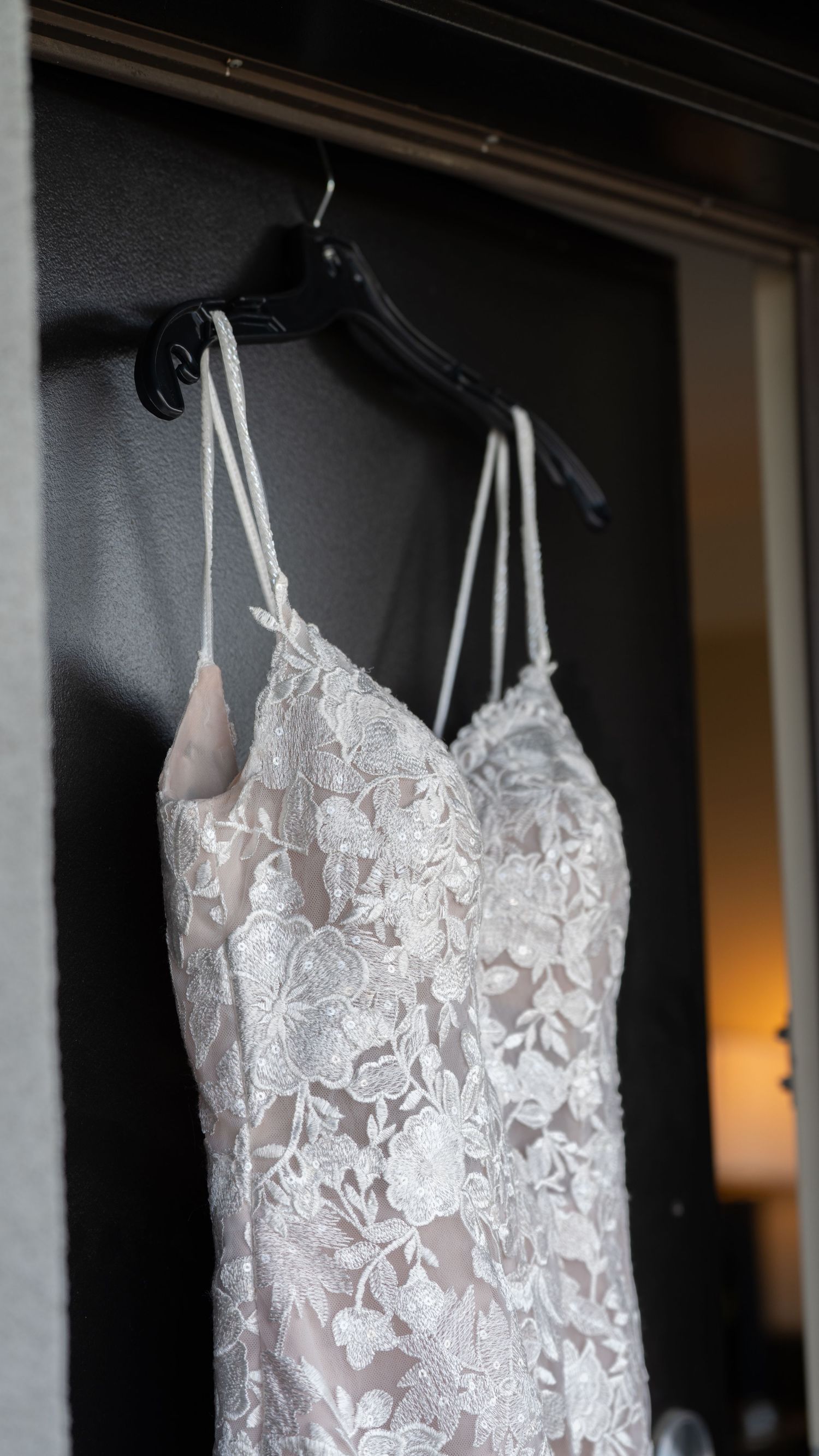 Elegant white lace wedding dress with intricate floral details hanging on display.