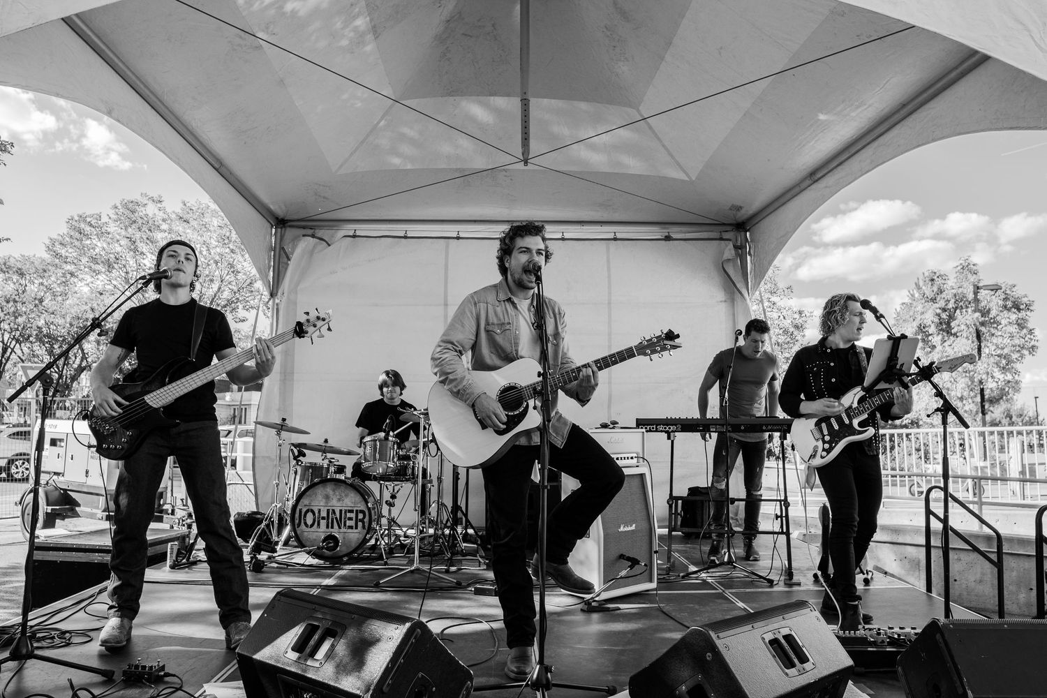 Black and white photo of full band performing under outdoor tent stage.