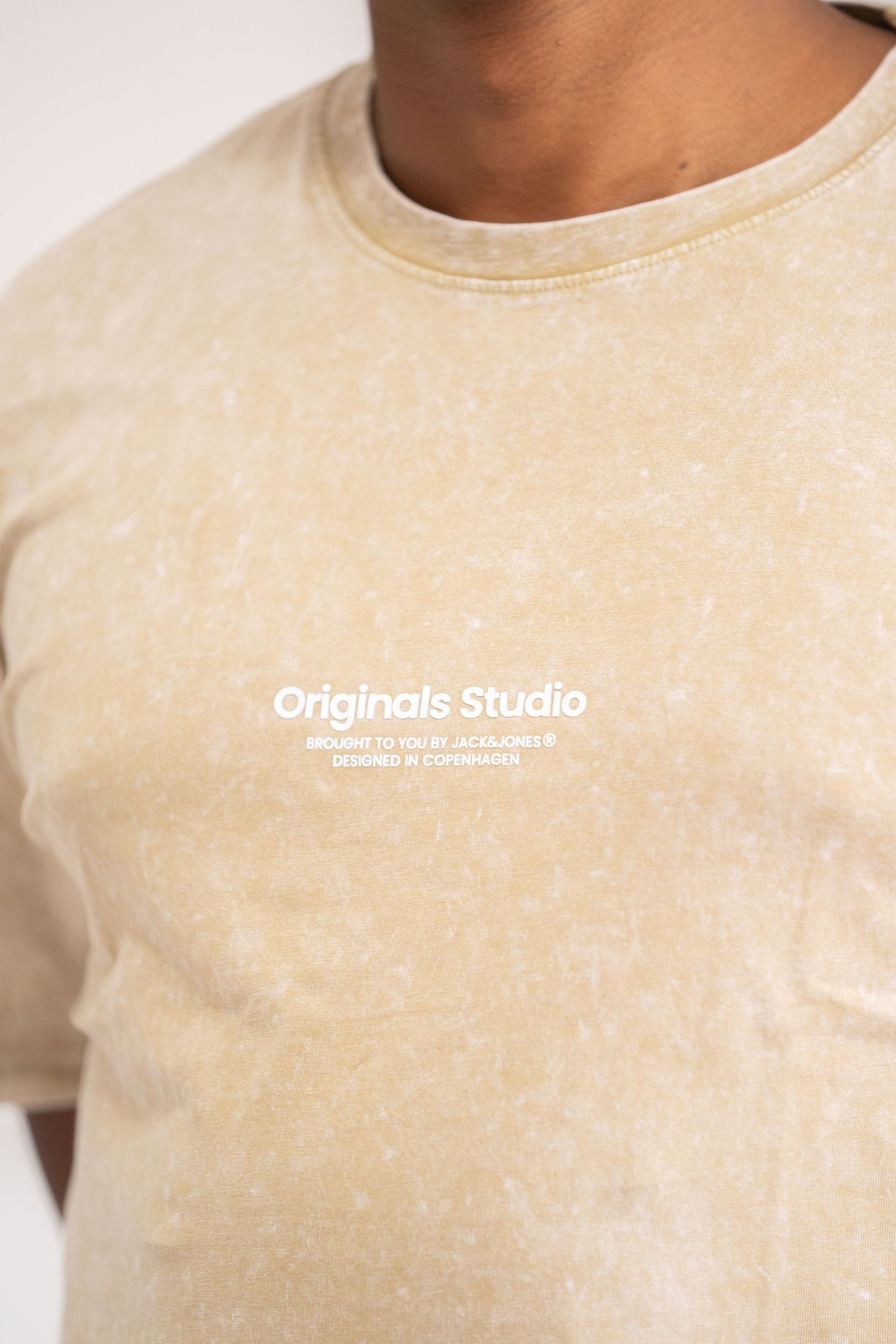 Close-up of beige t-shirt with Originals Studio text branding.