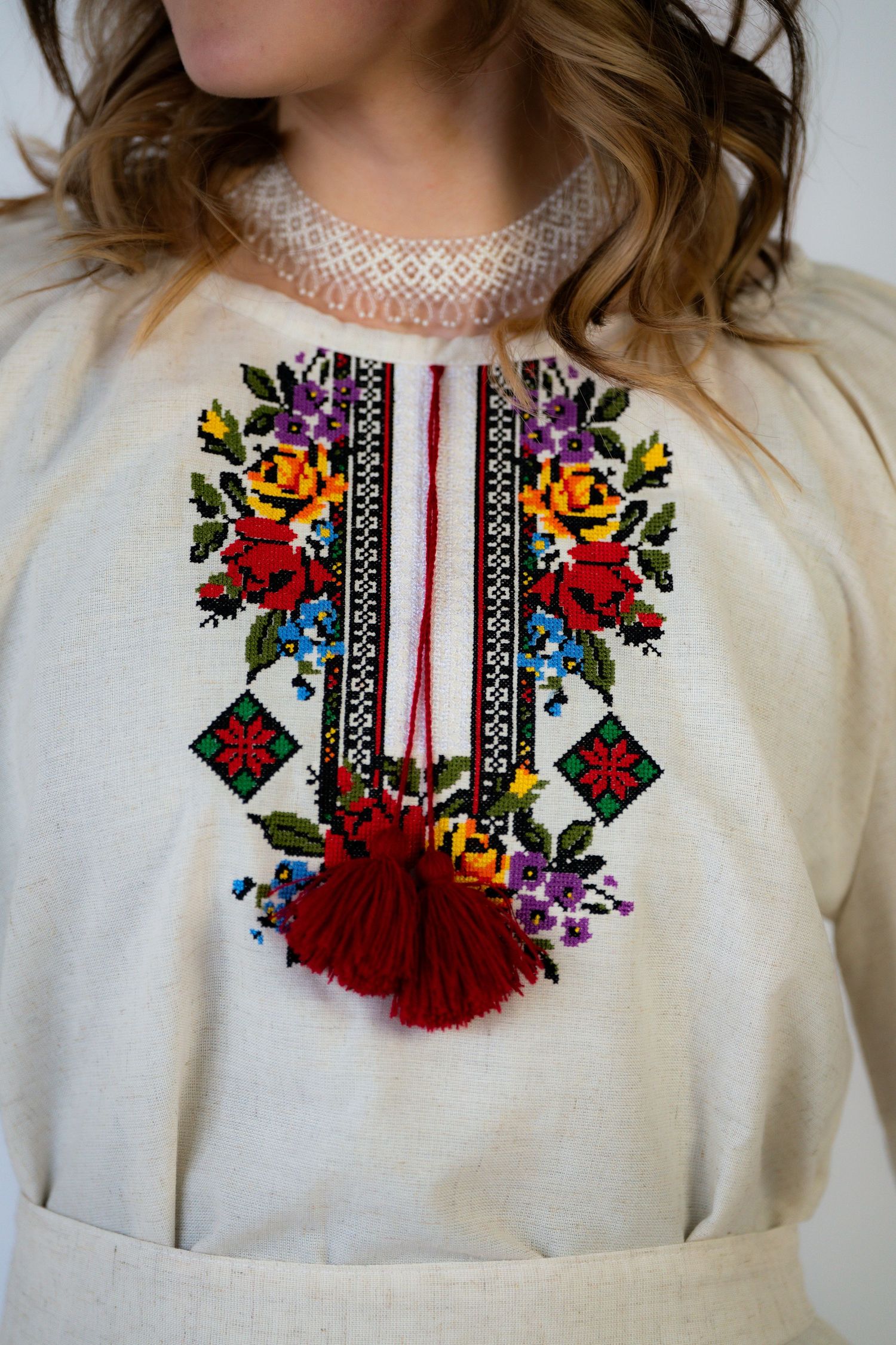 White blouse with colorful folk embroidery and red tassels around the neckline.