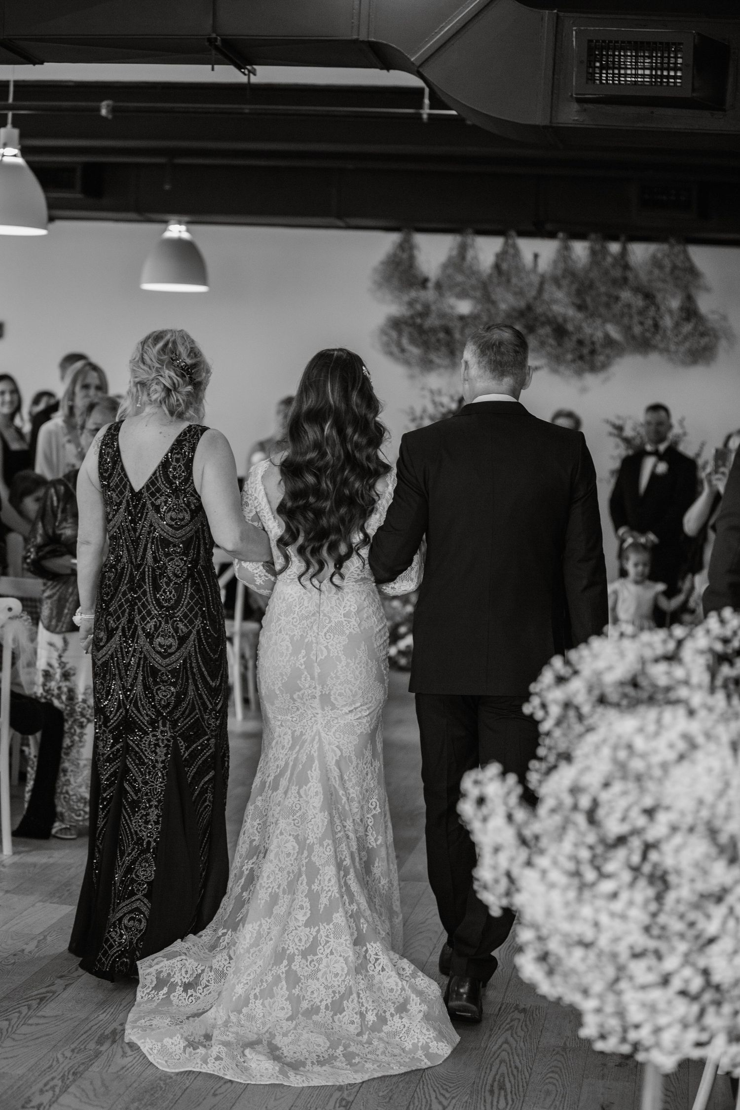 Wedding party in formal attire gathered around floral decorations in black and white.