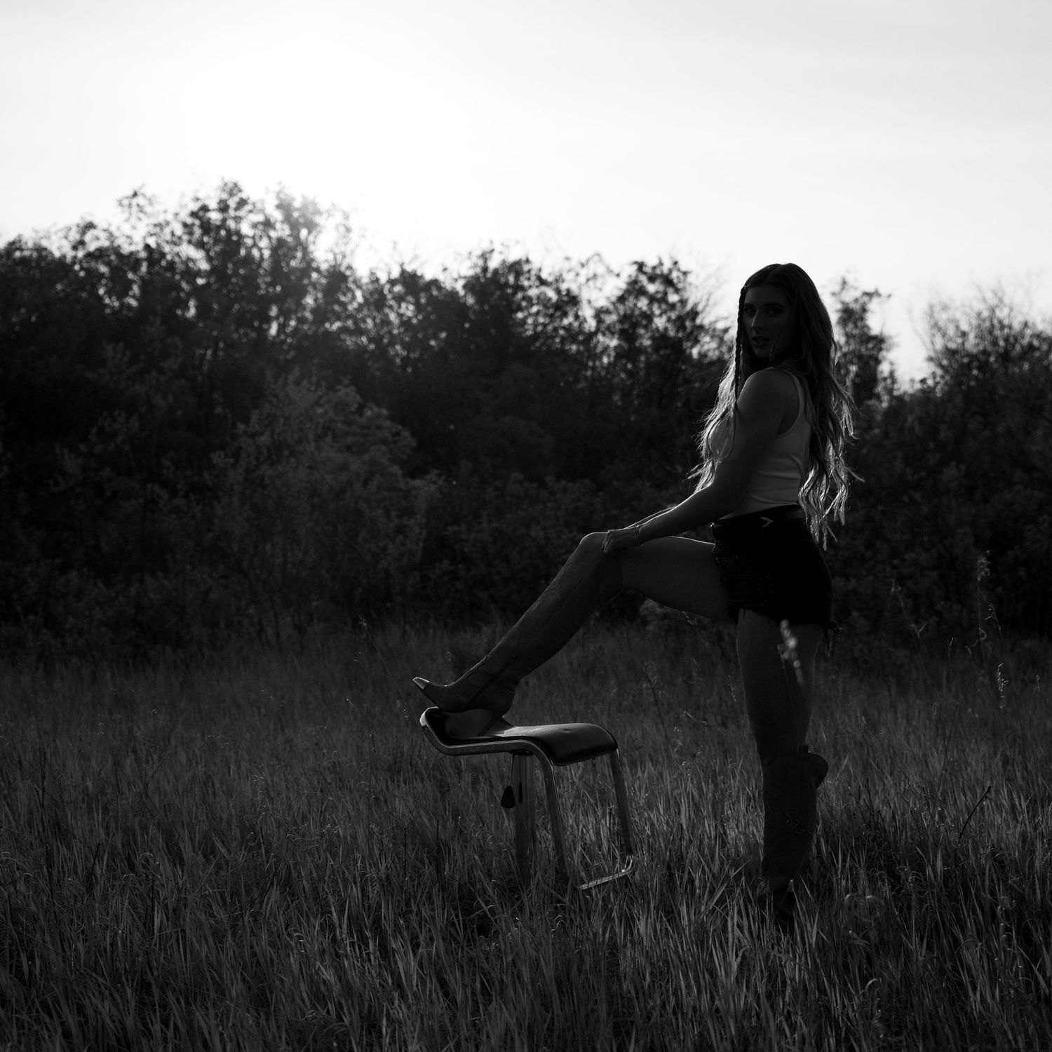 A silhouette of someone posing with a stool in a field at dusk.
