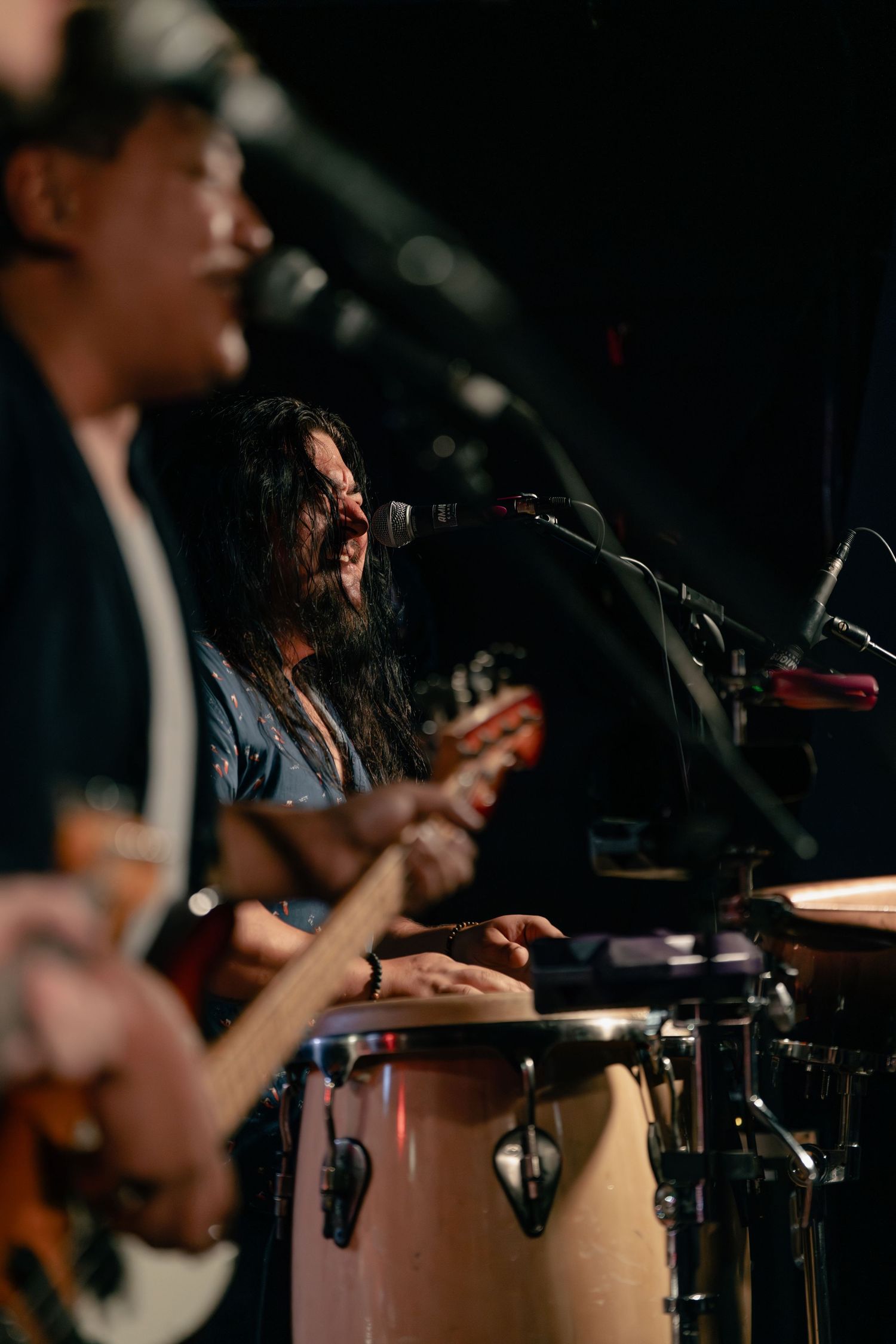 Musicians performing on stage with percussion instruments in dark atmospheric lighting.