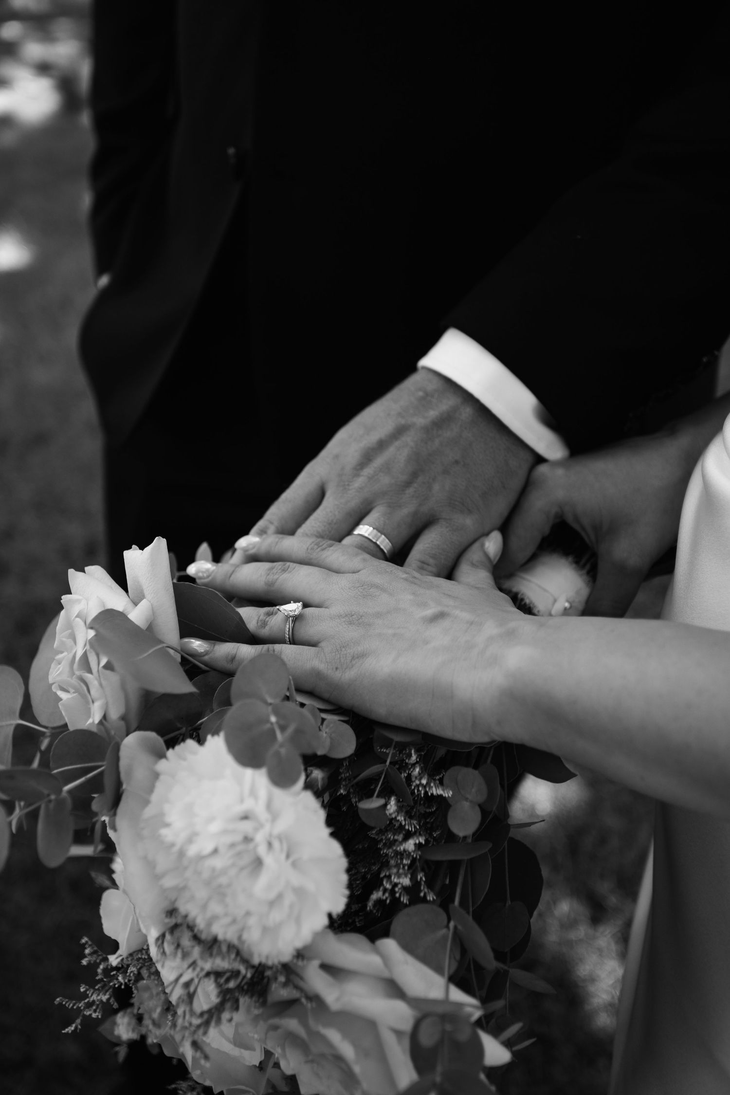Close up of wedding rings and hands with white floral bouquet in black and white.