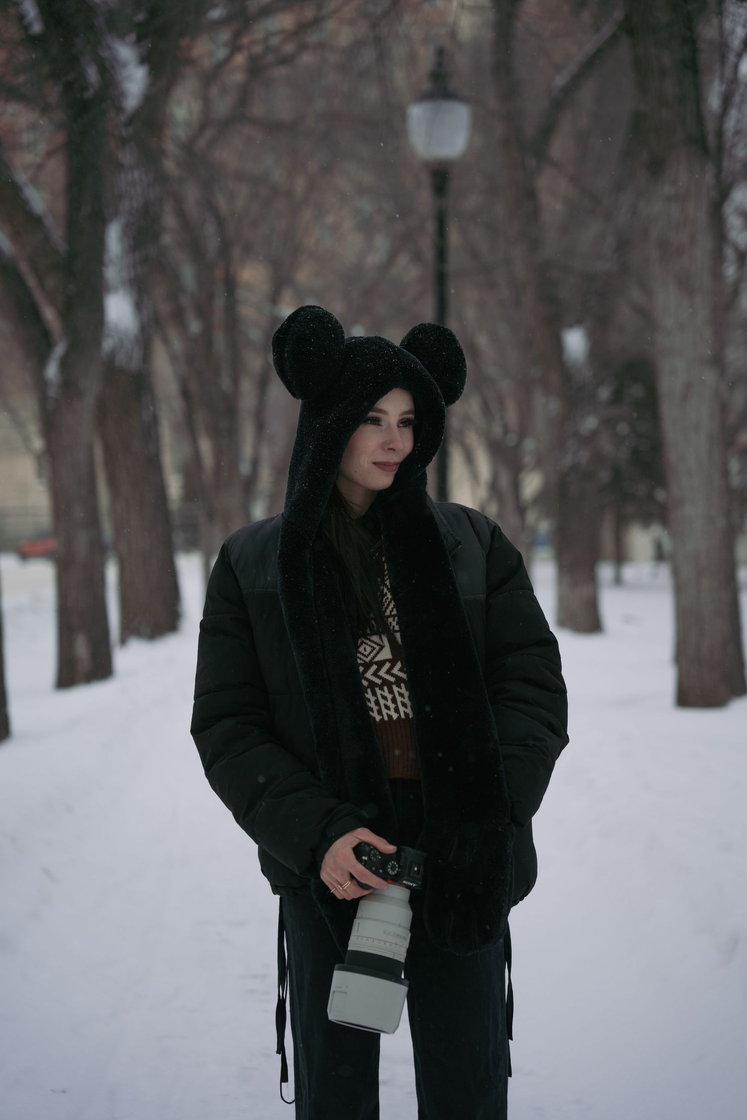 People walking through snowy park path wearing dark winter coats and hats.