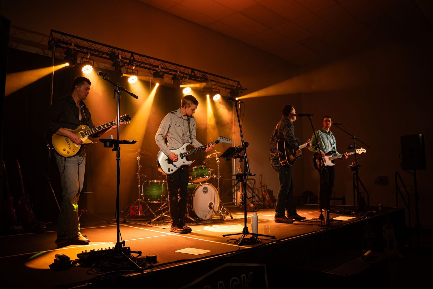 Wide concert stage shot with warm lighting and multiple musicians performing.