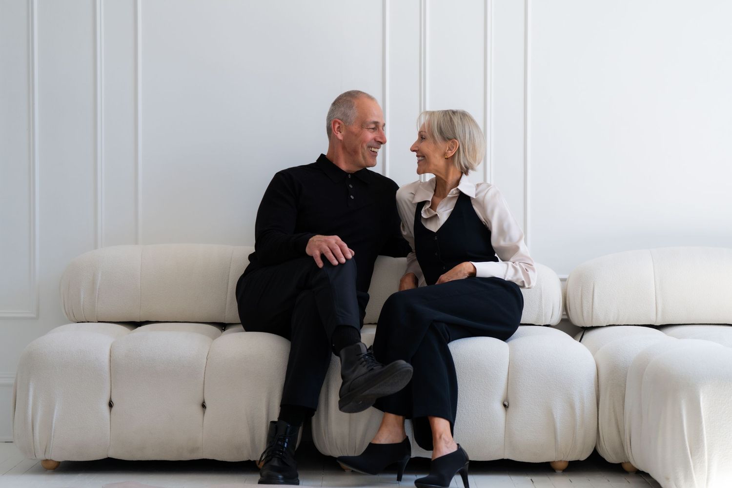 Two people having an animated conversation while seated on a modern white couch.
