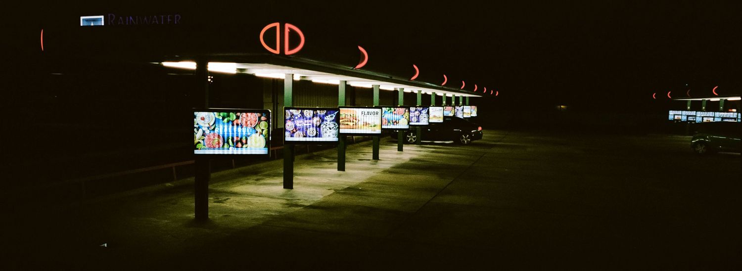Drive-in theater screens glowing at night with colorful movie displays illuminated against dark sky.