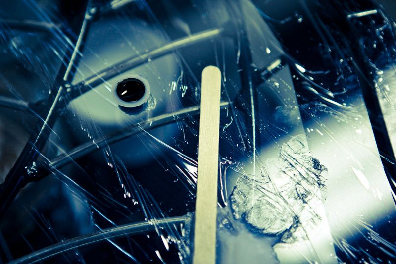 Close-up macro shot of broken glass with a wooden stick and dark metallic surface.
