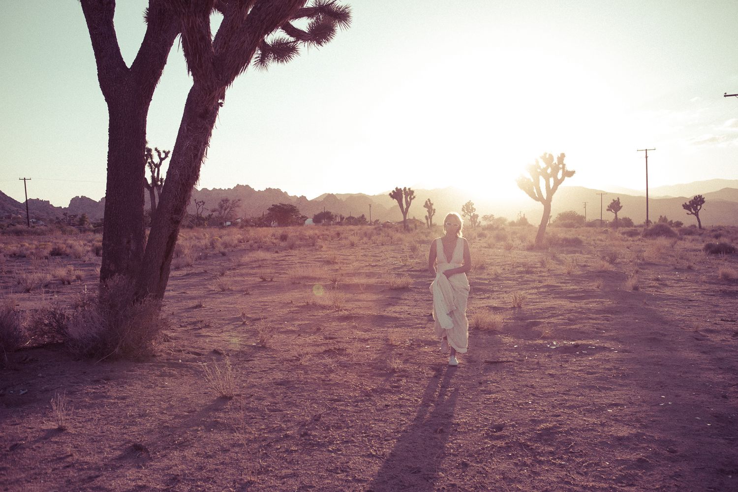 Woman in white dress walking through a sunlit Joshua Tree desert landscape at golden hour.