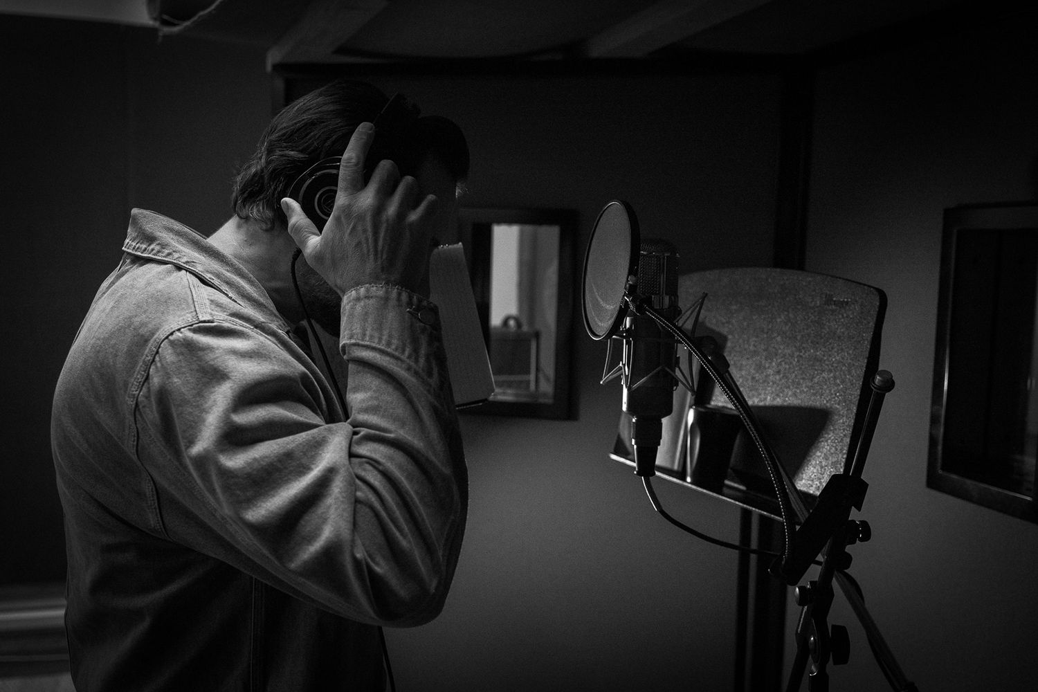 Black and white photo of a musician recording vocals in a professional studio.