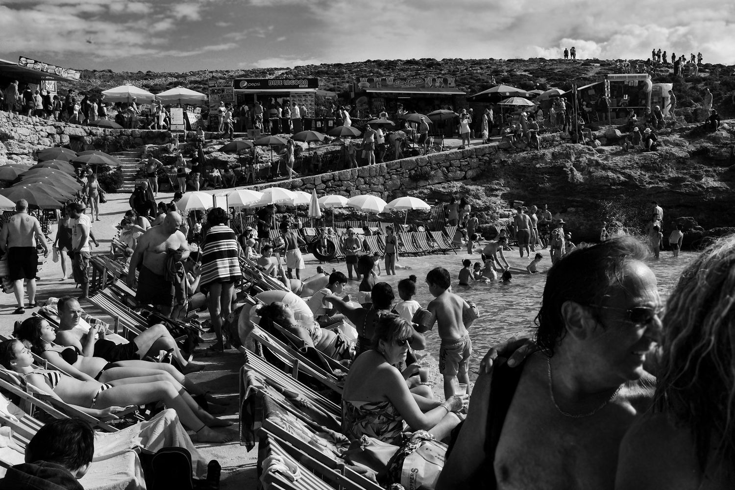 Black and white photo of a crowded beach scene with people sunbathing and swimming.