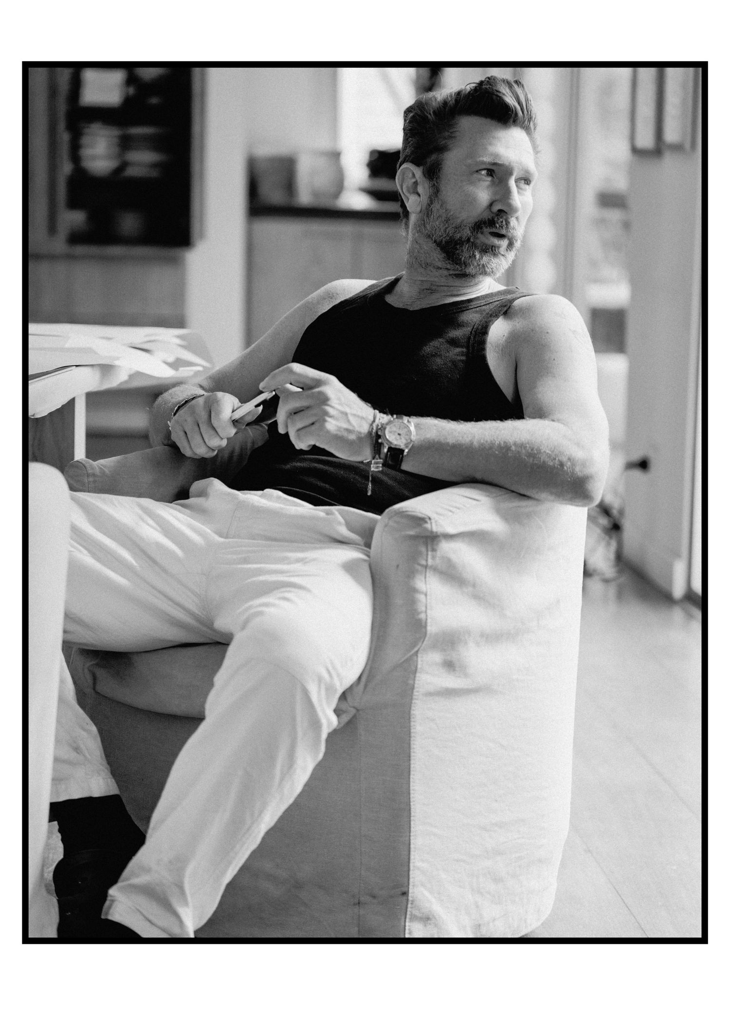 Bearded man in black tank top relaxing in armchair, black and white portrait.