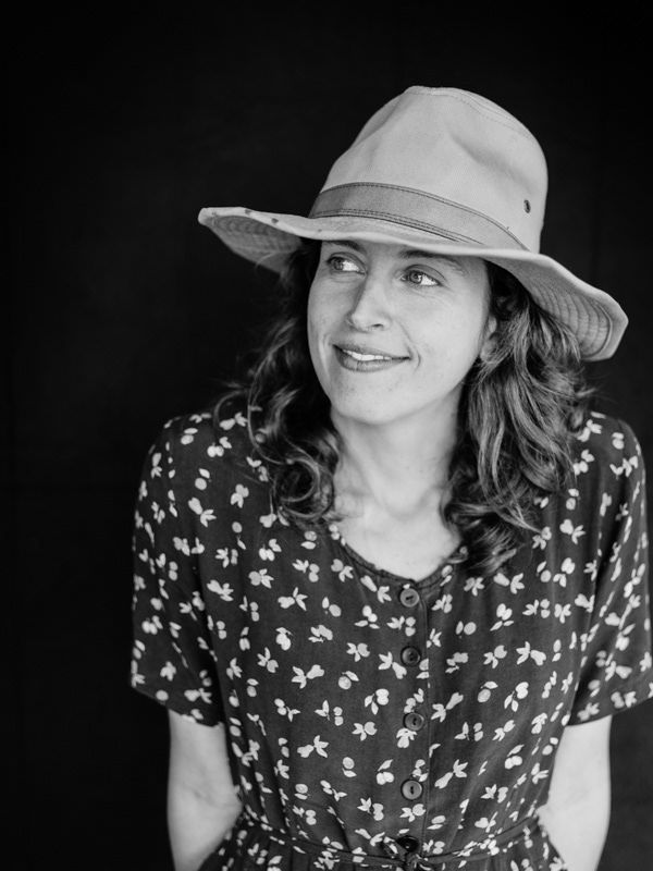 Black and white portrait of smiling woman in floral dress and wide-brim hat.