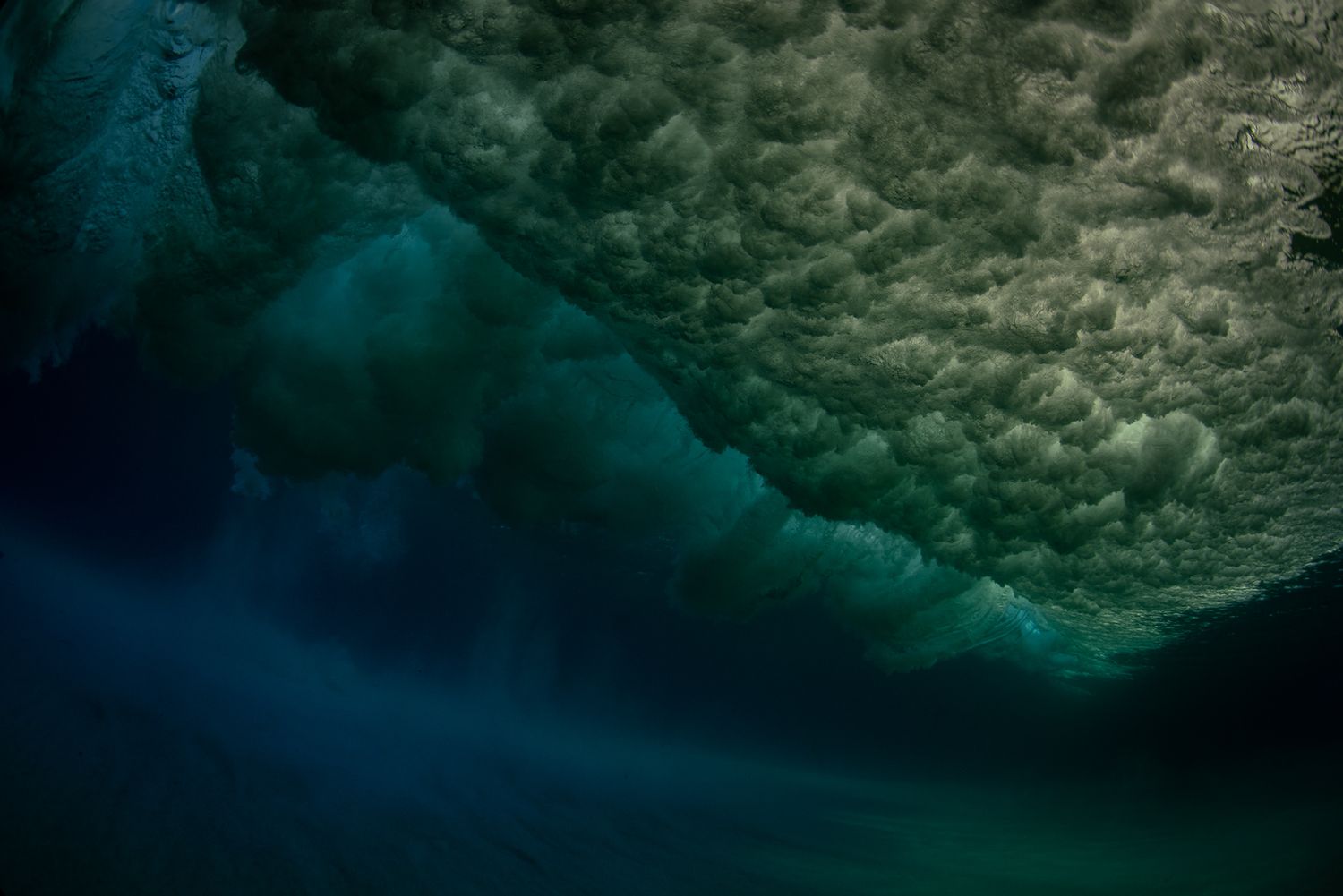 Underwater view of a powerful ocean wave crashing in deep teal water.