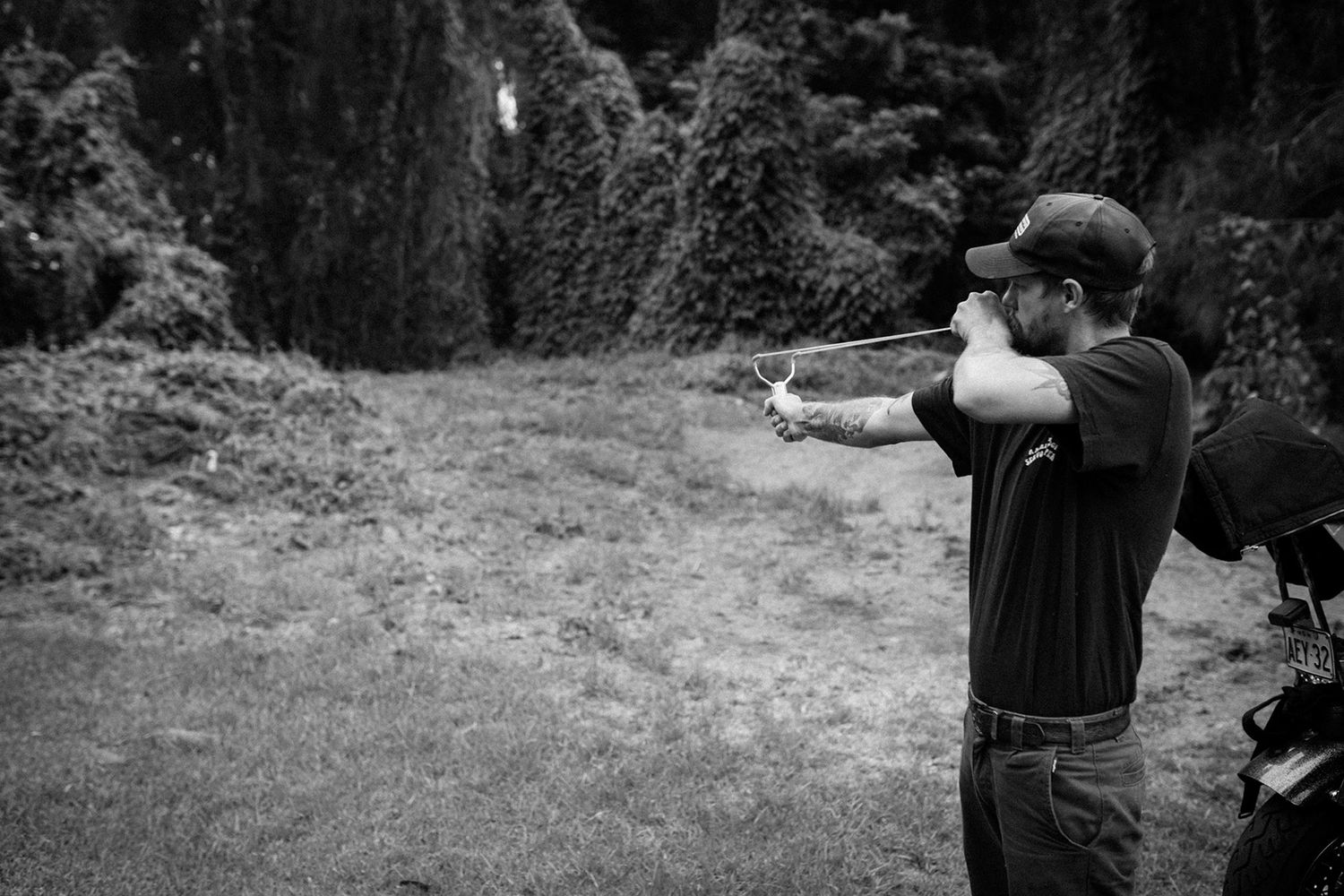 Black and white photo of a man aiming a bow and arrow in an outdoor setting.