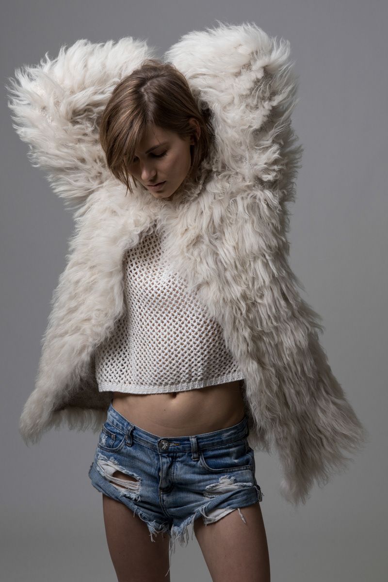 Woman in white fluffy fur coat and denim cutoff shorts posing in studio.