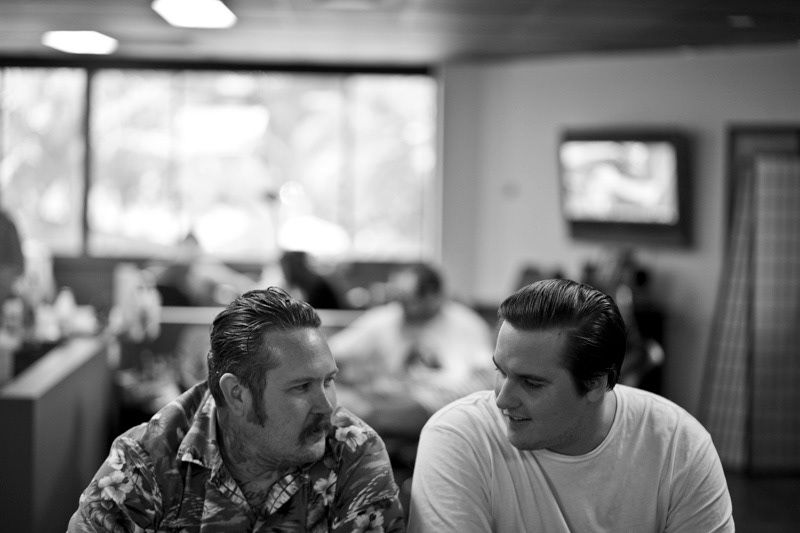 Two men having a conversation in a casual indoor setting, captured in black and white photography.