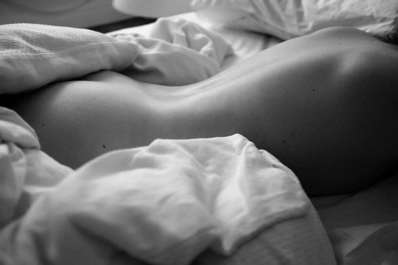 Black and white artistic close-up of human body curves on white sheets.