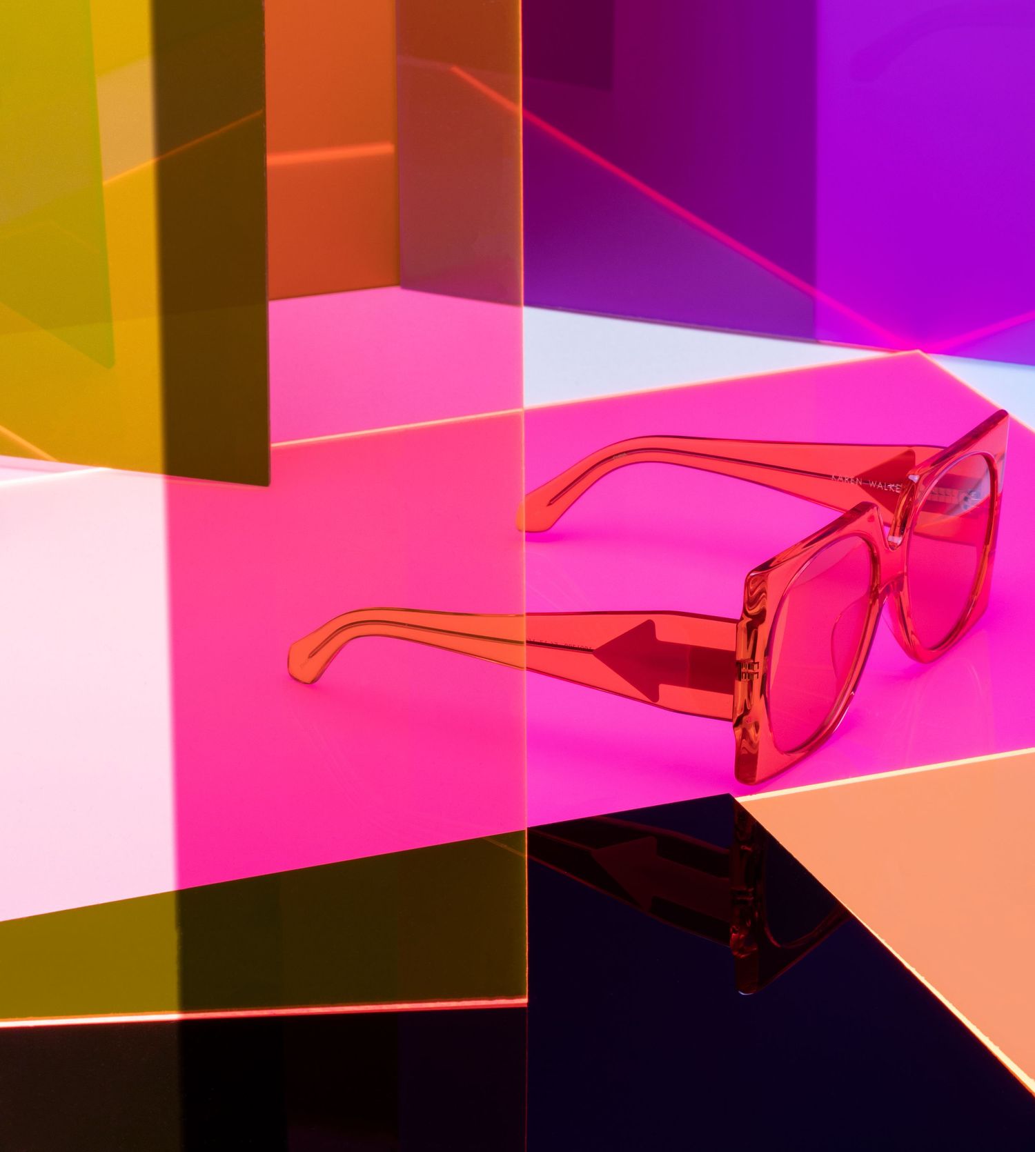 Transparent pink square sunglasses displayed against vibrant multicolored neon acrylic panels.