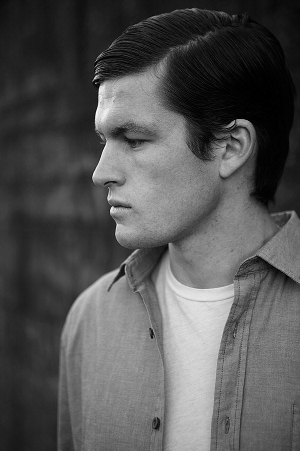 A black and white profile portrait of a young man in a button-up shirt looking downward.