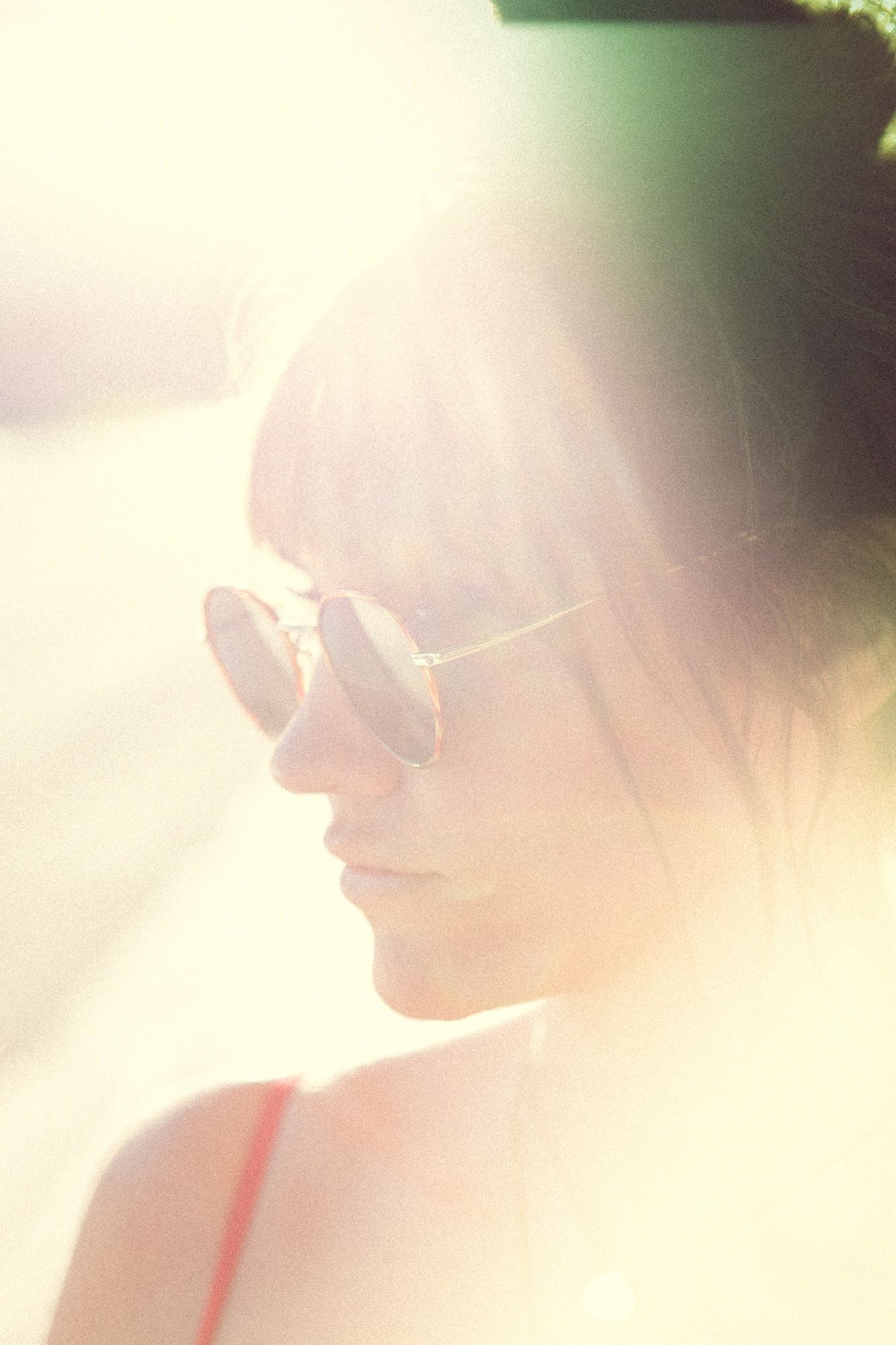 Woman with bangs wearing aviator sunglasses in warm sunlight lens flare portrait.