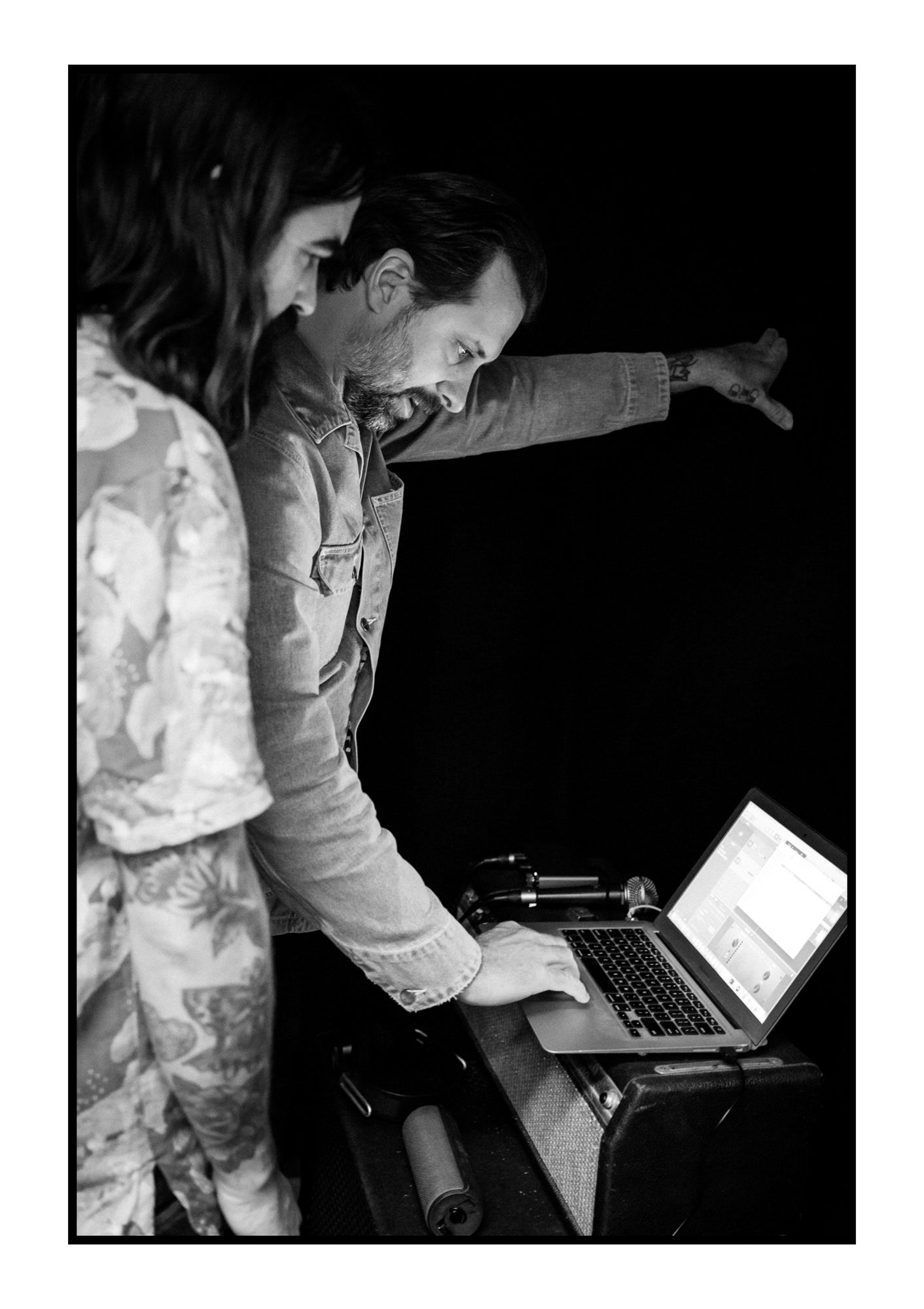 Man and woman laughing while using laptop at DJ booth in black and white.