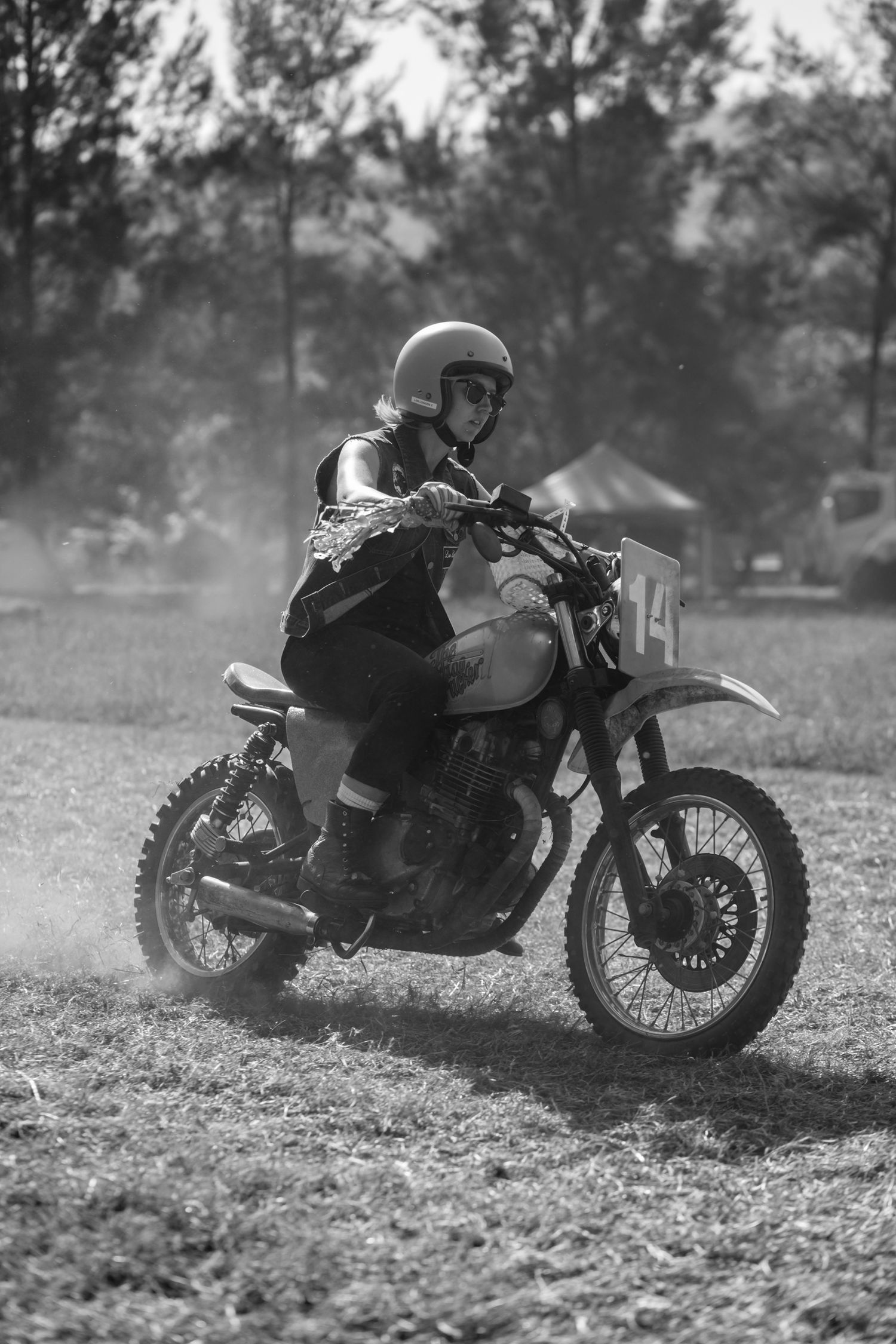 Black and white photo of a motocross rider racing on a dirt track kicking up dust.