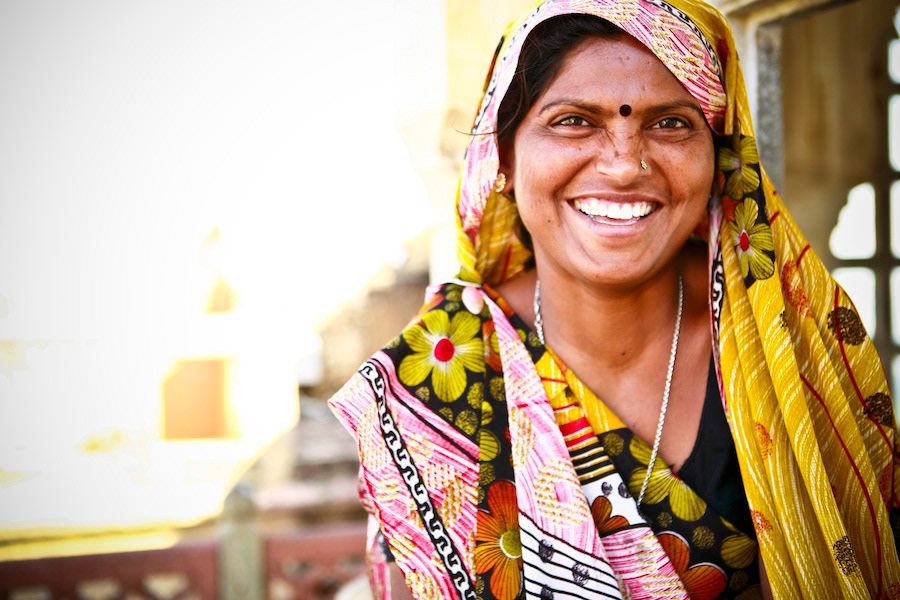 Smiling Indian woman in colorful floral sari and traditional bindi in bright sunlight.