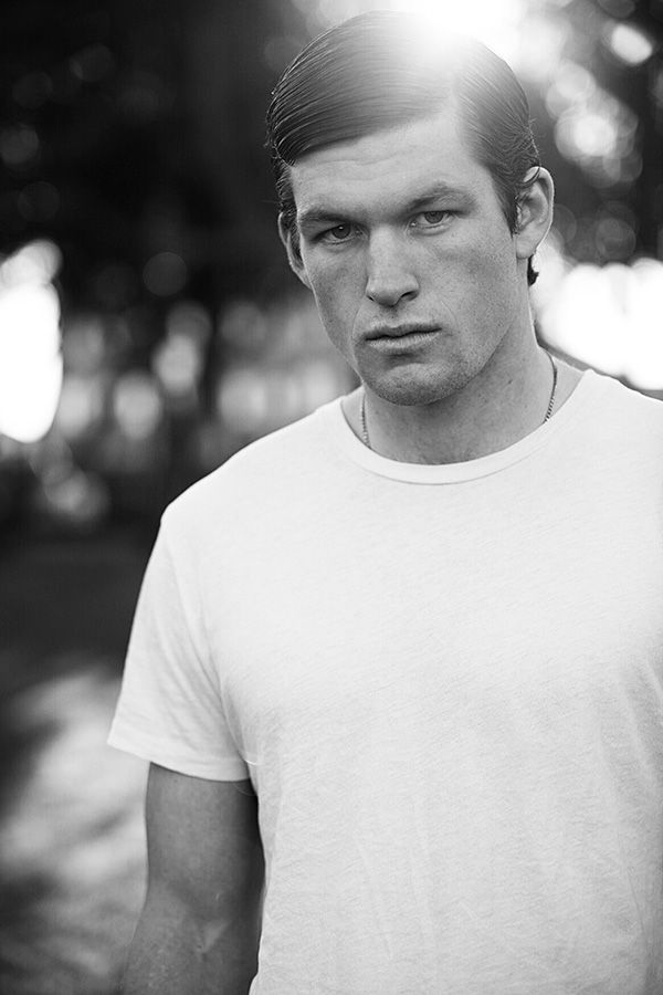 Black and white portrait of a young man in a white t-shirt with sunlight behind him outdoors.