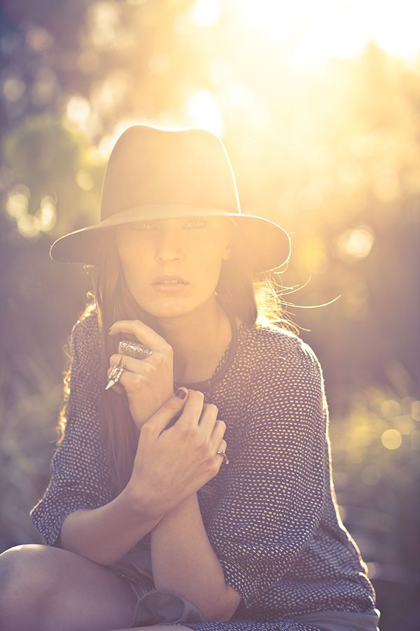 Young woman wearing a wide-brim hat holding a book in warm golden sunlight outdoors.
