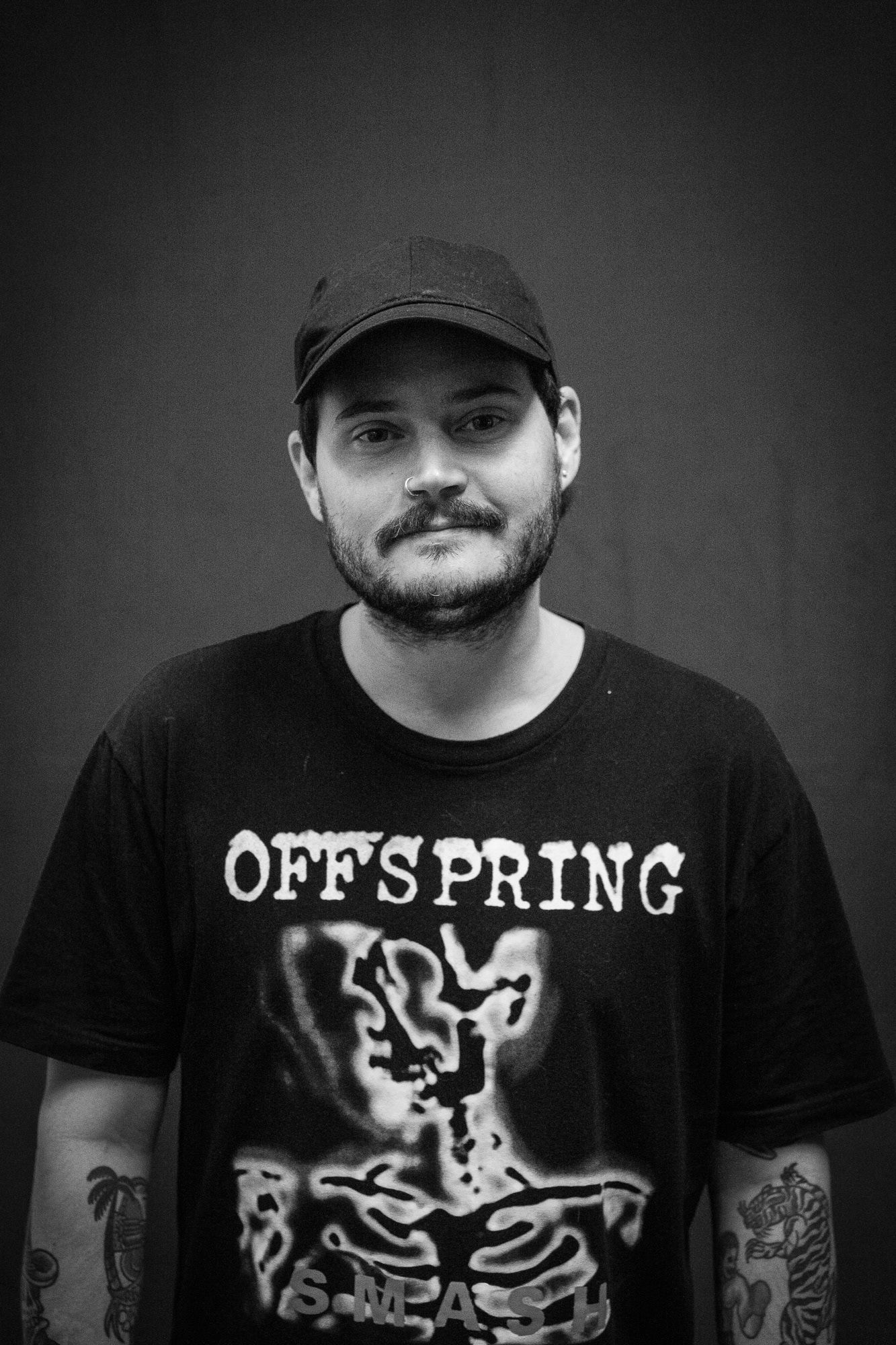 Man wearing Offspring band tee and cap with tattoos in black and white portrait.