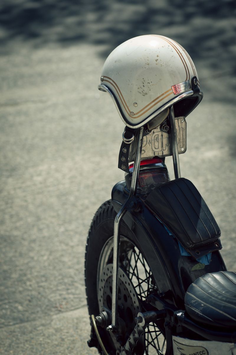 Vintage white motorcycle helmet resting on the rear of a classic cafe racer bike.