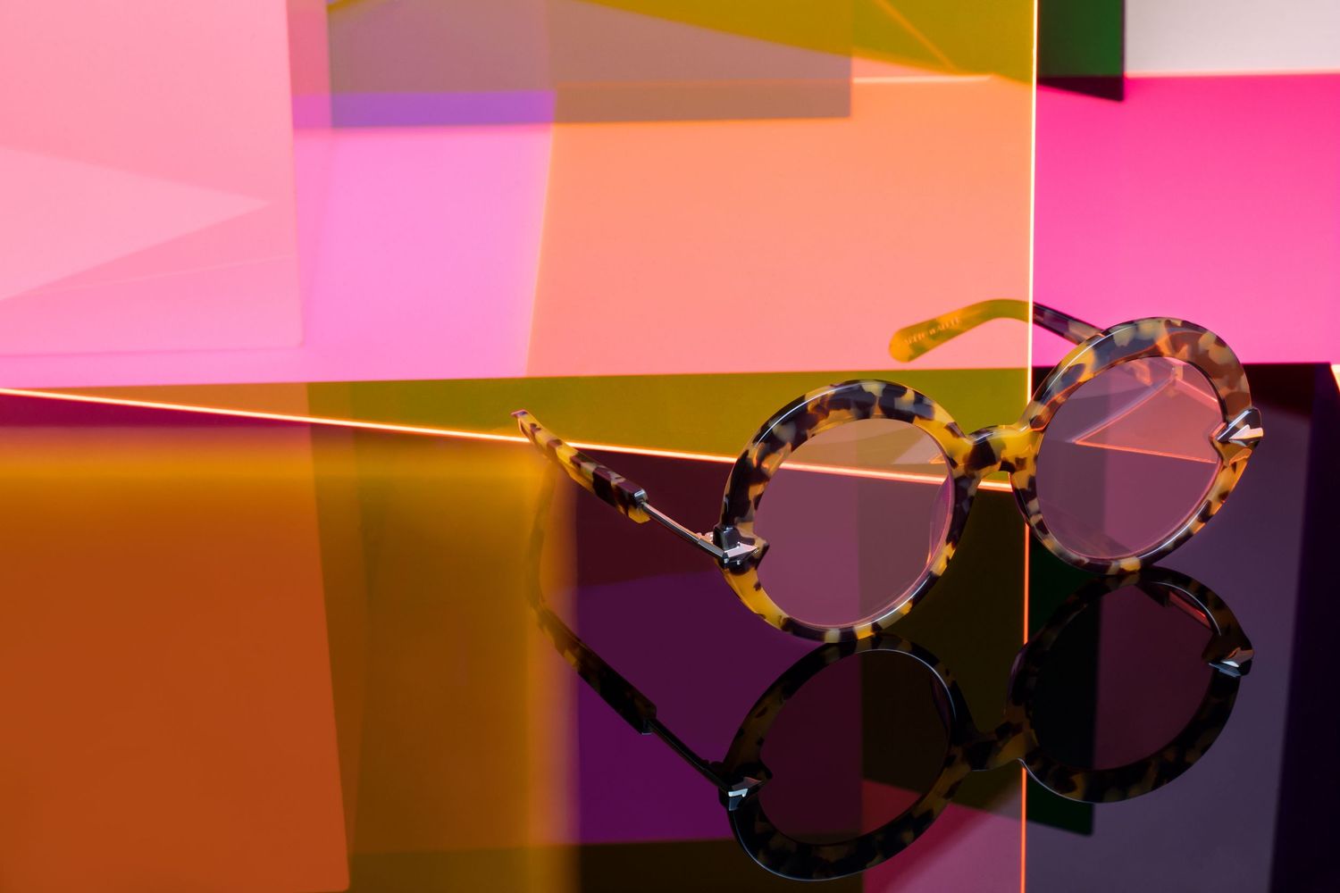Tortoiseshell round sunglasses resting against colorful pink and yellow transparent acrylic panels.