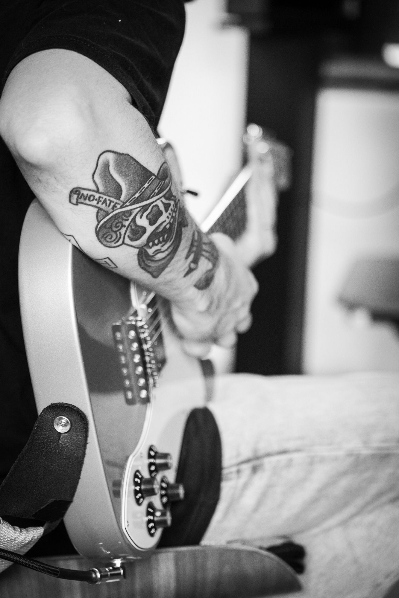 Black and white close-up of tattooed arm holding electric guitar.