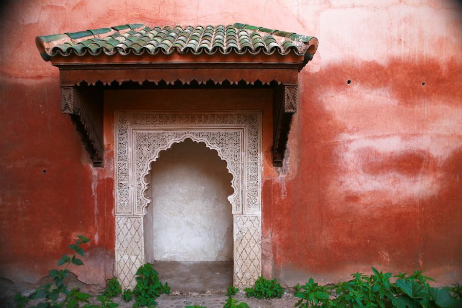 Ornate Moroccan arch niche with intricate white plasterwork carved details set against a vibrant red wall.