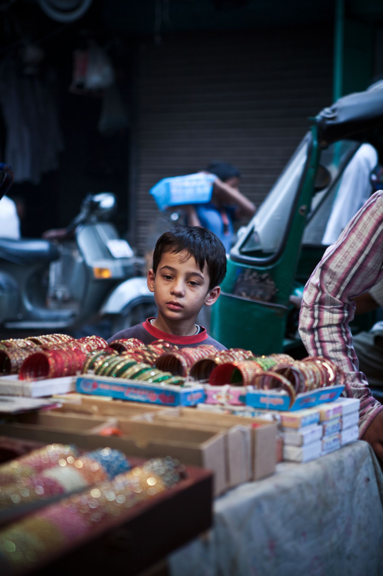 Young Indian boy examining colorful bangles and jewelry at a vibrant street market stall.