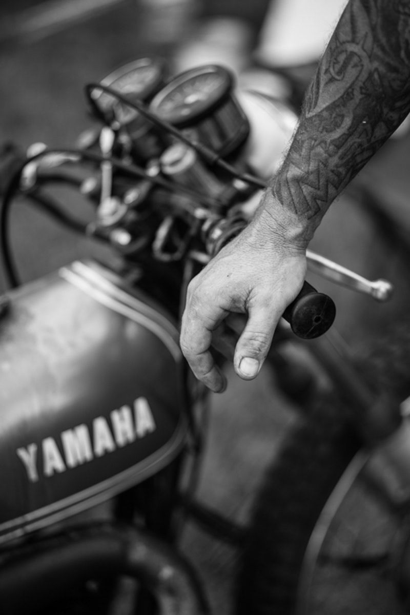 Tattooed hand resting on the handlebar of a vintage Yamaha motorcycle in black and white.