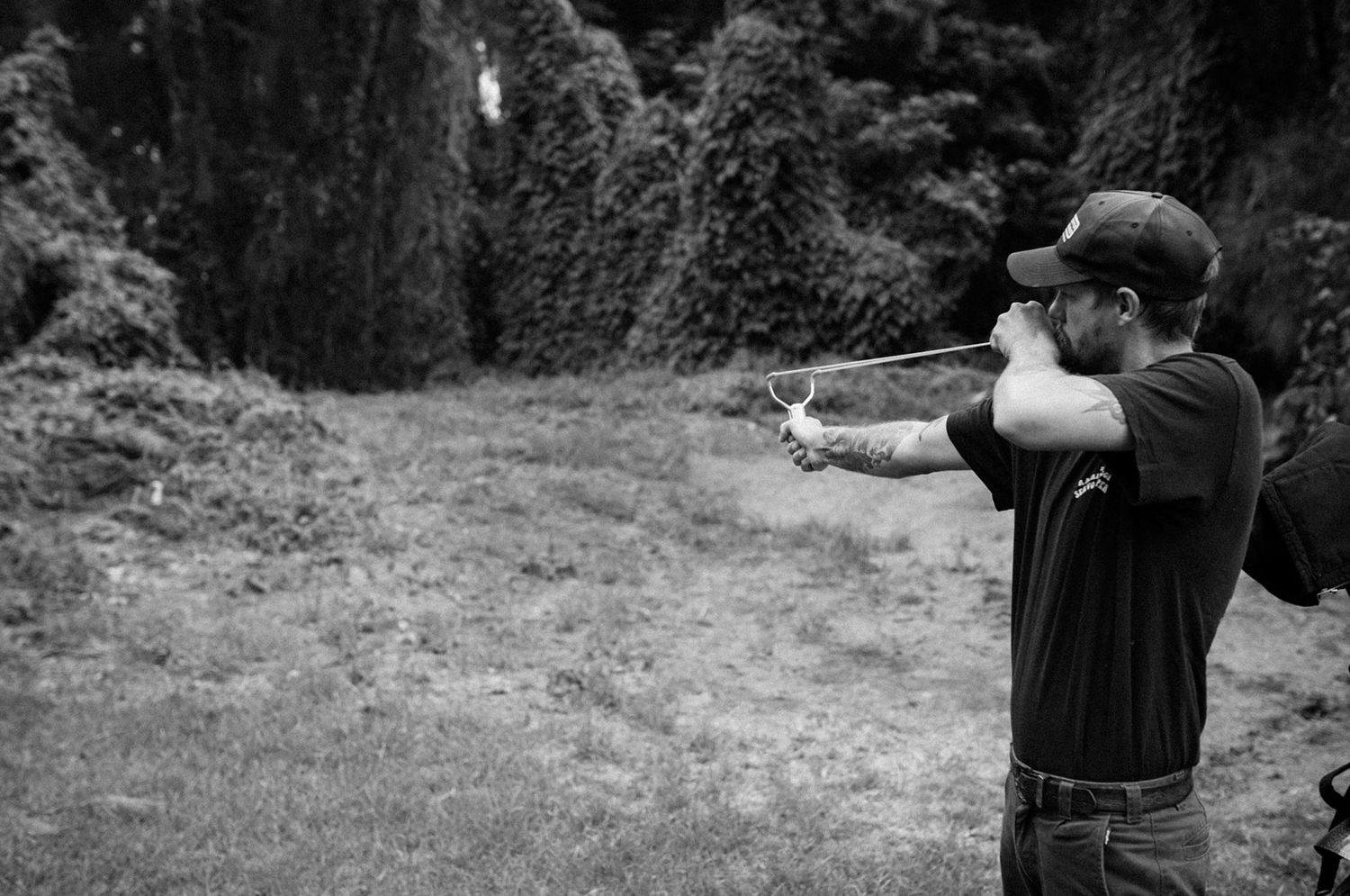Man aiming a slingshot outdoors in black and white photography.