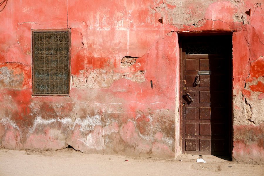 Weathered red ochre building exterior with a wooden door and barred window in North Africa.