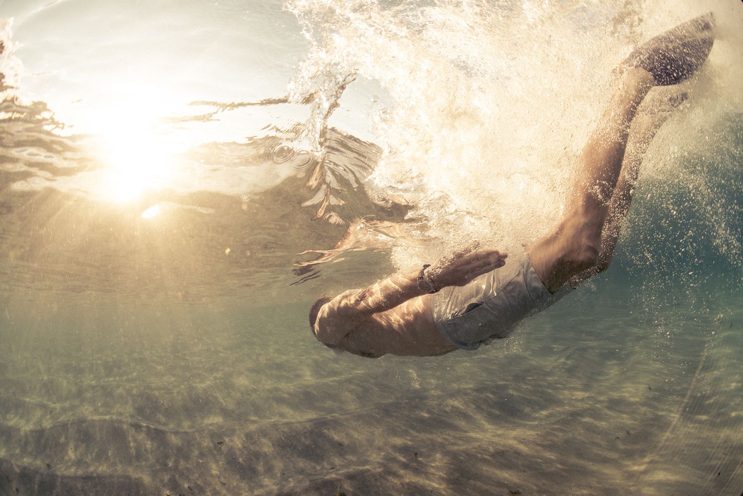 Underwater shot of a swimmer diving into sunlit clear water with golden light.